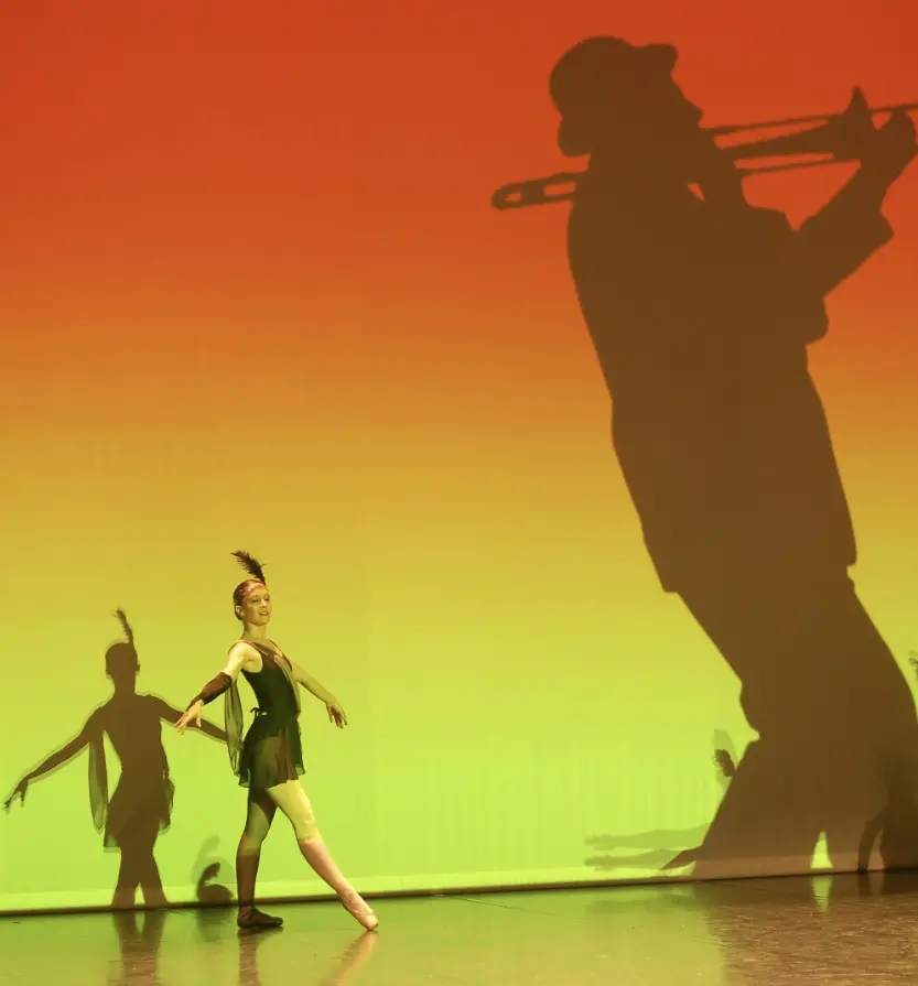 Danseuse en costume vert sur fond de scène orange et vert avec ombre projetée d'un musicien au trombone, spectacle de danse, Bezons — juin 2011